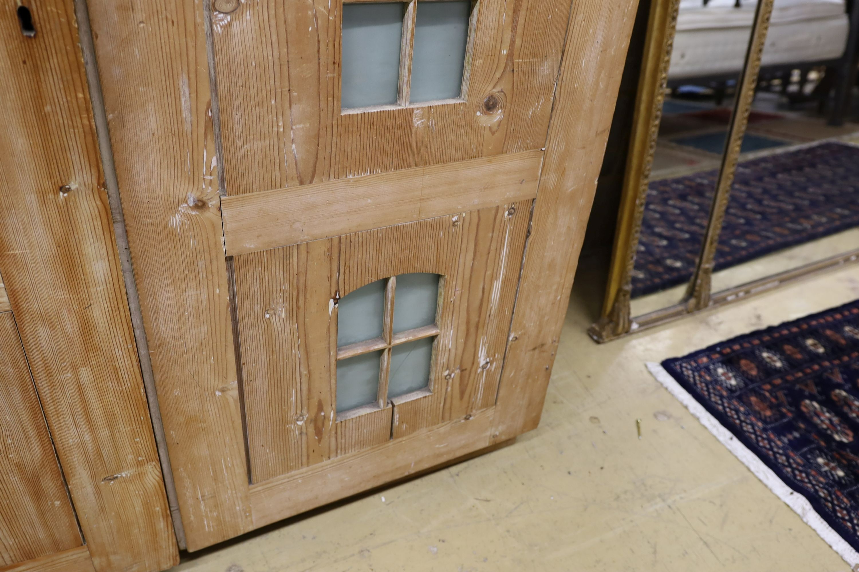A 19th century stripped pine hall cupboard modelled as a dolls house the two door nine window facade enclosing a compartmented interior, width 182cm, depth 46cm, height 192cm